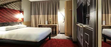 A hotel room with a bed, a desk, a TV, and a wardrobe.