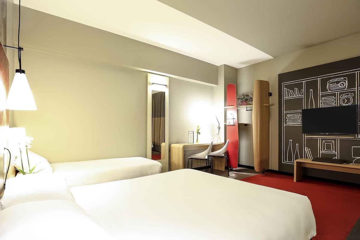 A hotel room with two beds, a desk, a chair, a TV, and a wall with a chalkboard design.