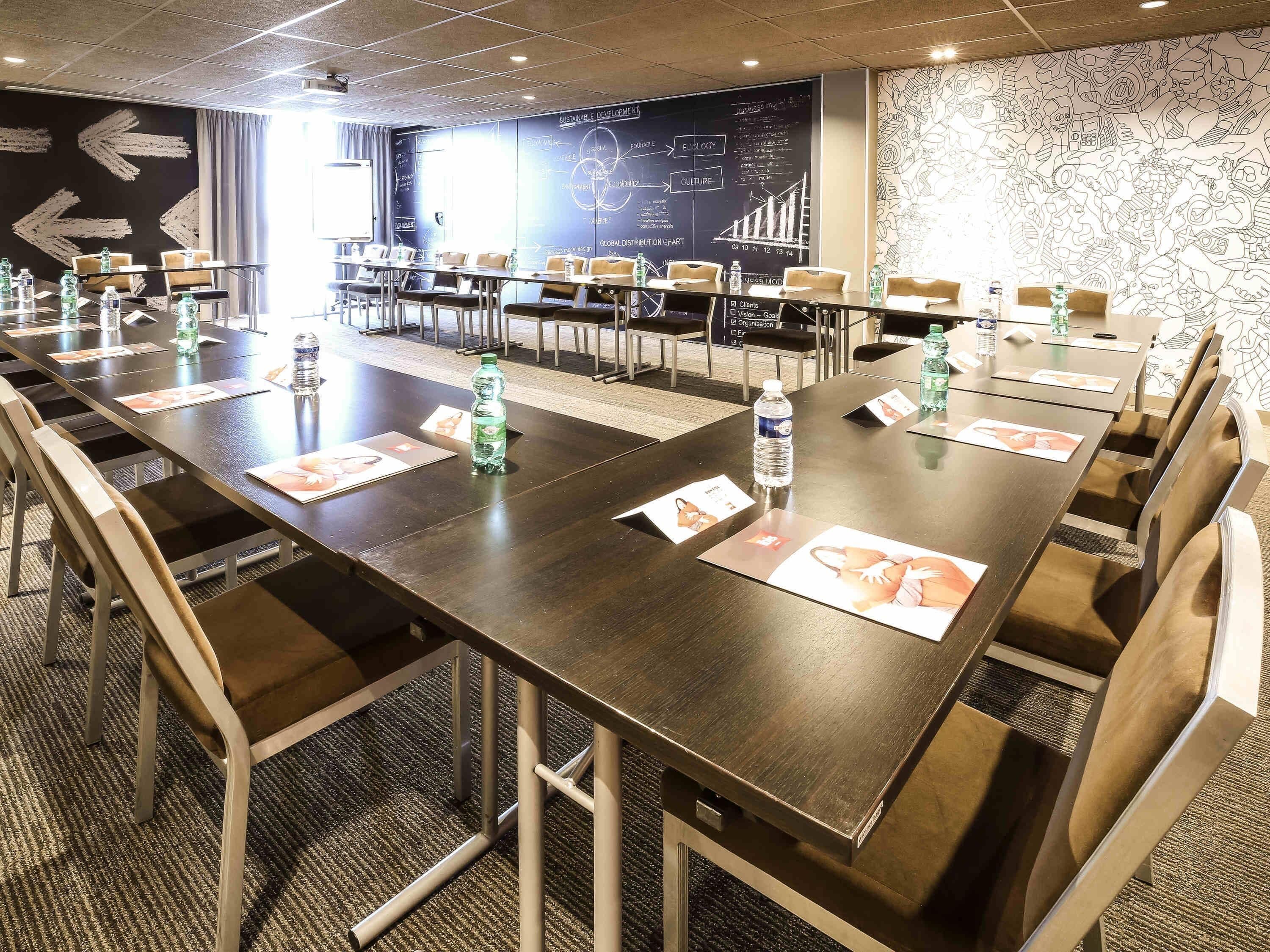 A conference room with long tables, chairs, water bottles, and informational cards.