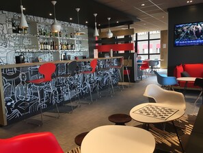 Eine moderne Bar mit einer Schwarz-Weiß-Wandmalerei, roten und blauen Stühlen und einem Fernseher, der Nachrichten zeigt.