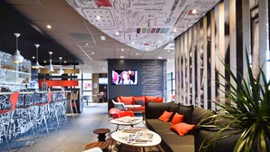 Un espace bar moderne avec des tabourets hauts, un canapé avec des coussins orange et un écran de télévision.
