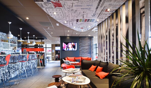 Eine moderne Bar mit hohen Hockstühlen, einem Sofa mit orangefarbenen Kissen und einem Fernsehbildschirm.