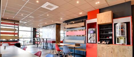 A modern cafe with a long communal table, individual seating, and a coffee machine.