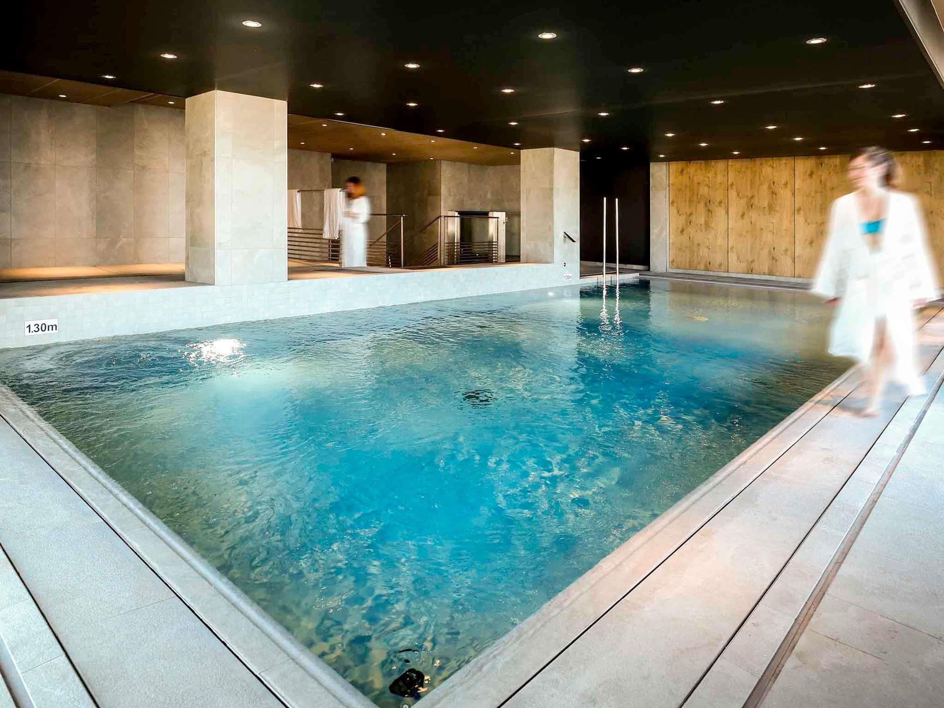 An indoor swimming pool with clear water, a wooden deck, and a modern architectural design.