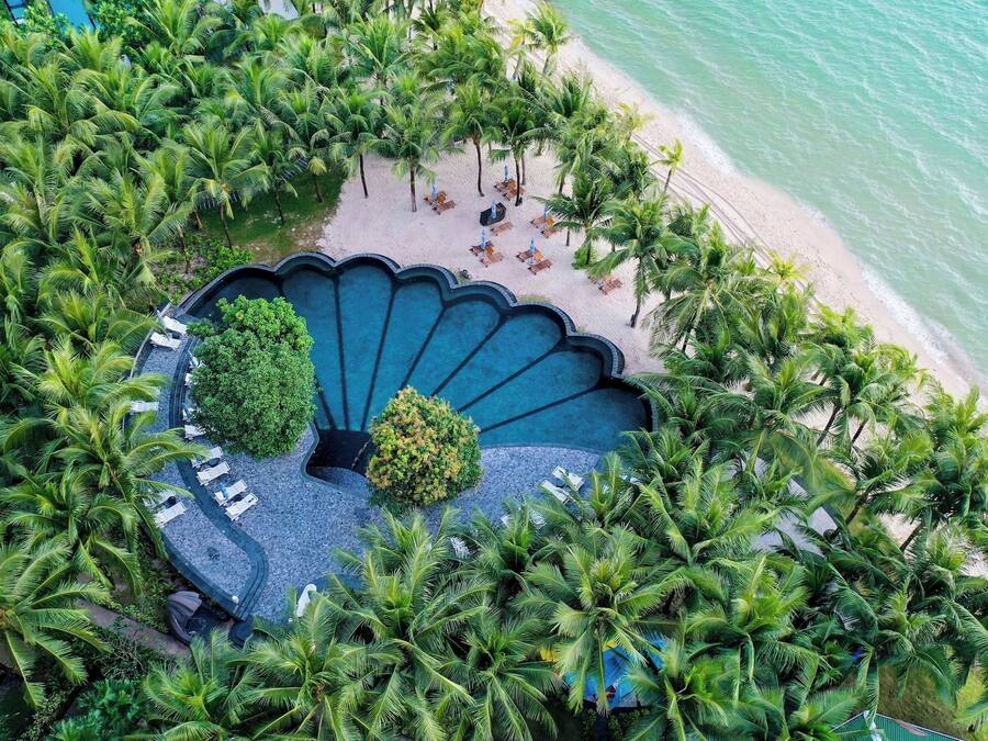An aerial view of a resort with a circular infinity pool surrounded by palm trees and beach chairs.