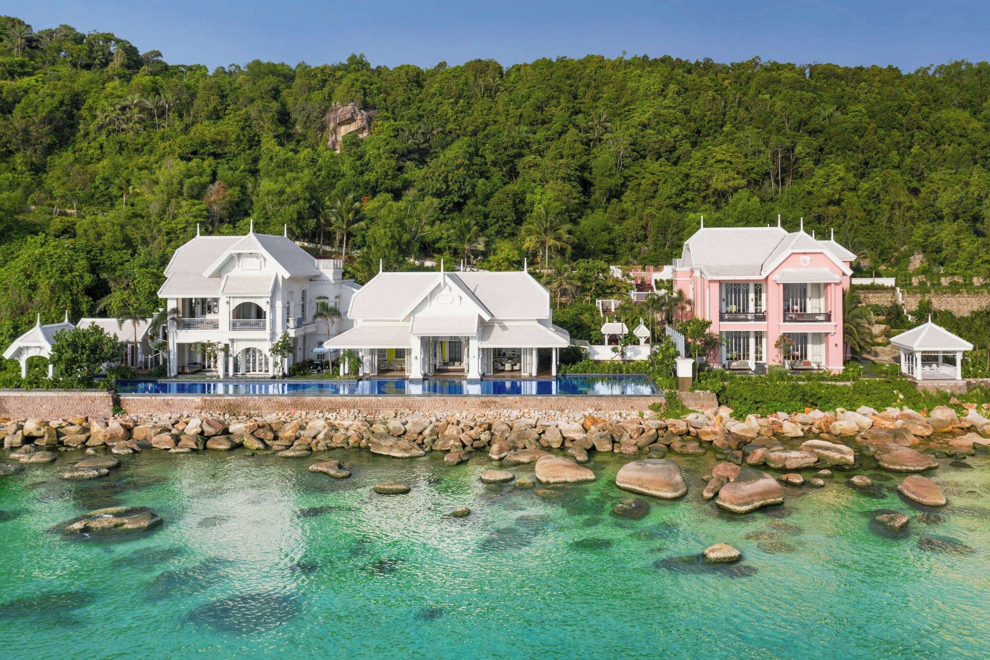 Una propiedad costera con varias villas blancas y rosas, una piscina y un litoral rocoso.