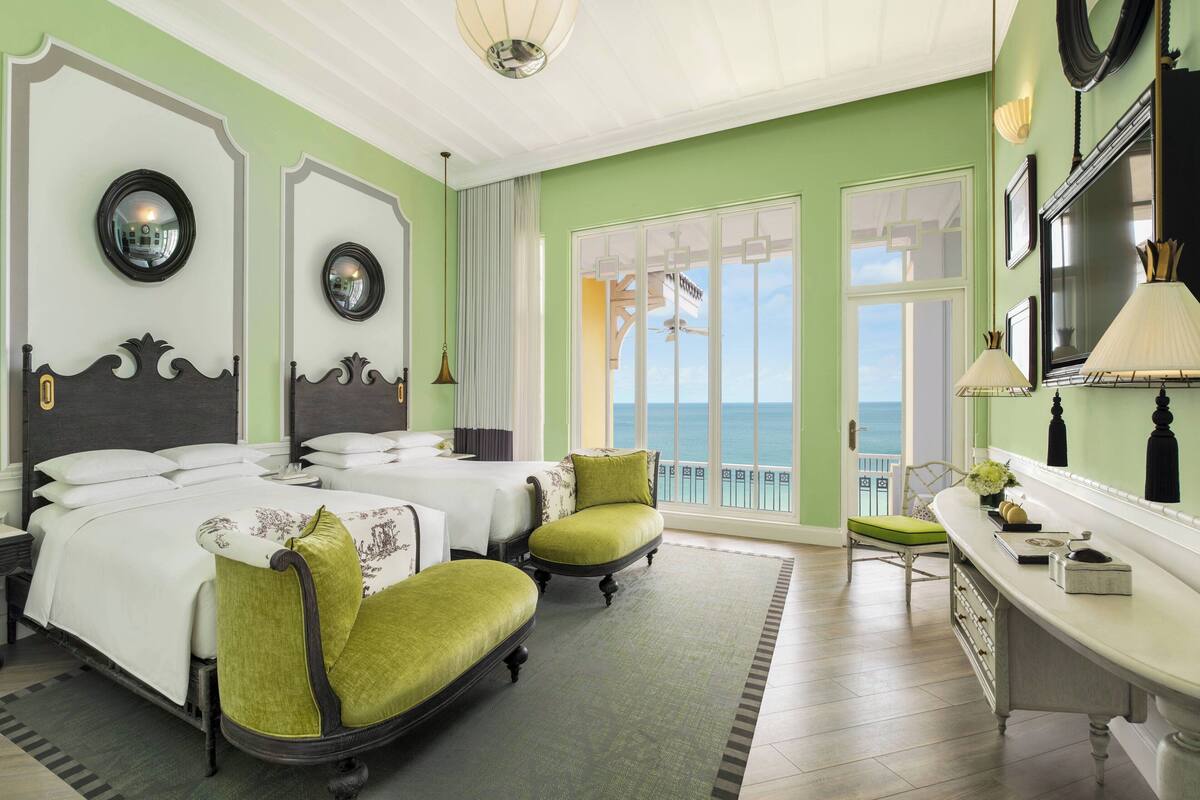 Ein Hotelzimmer mit Bett, zwei Stühlen, einem Schreibtisch und Meerblick.