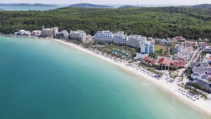 Ein Küstenort mit Strandvillen, einem Sandstrand und einer dichten Wald- und Hügelkulisse.