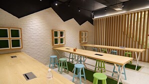 Een moderne eetruimte met houten tafels en groene krukken, met een bakstenen muur en een schuin dak.