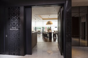 La entrada a un comedor llamado 'Sakura', con una decoración moderna, que incluye una mesa central y sillas, y un techo con iluminación empotrada.