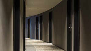 Un pasillo con piso alfombrado, paredes oscuras y puertas que dan a habitaciones.