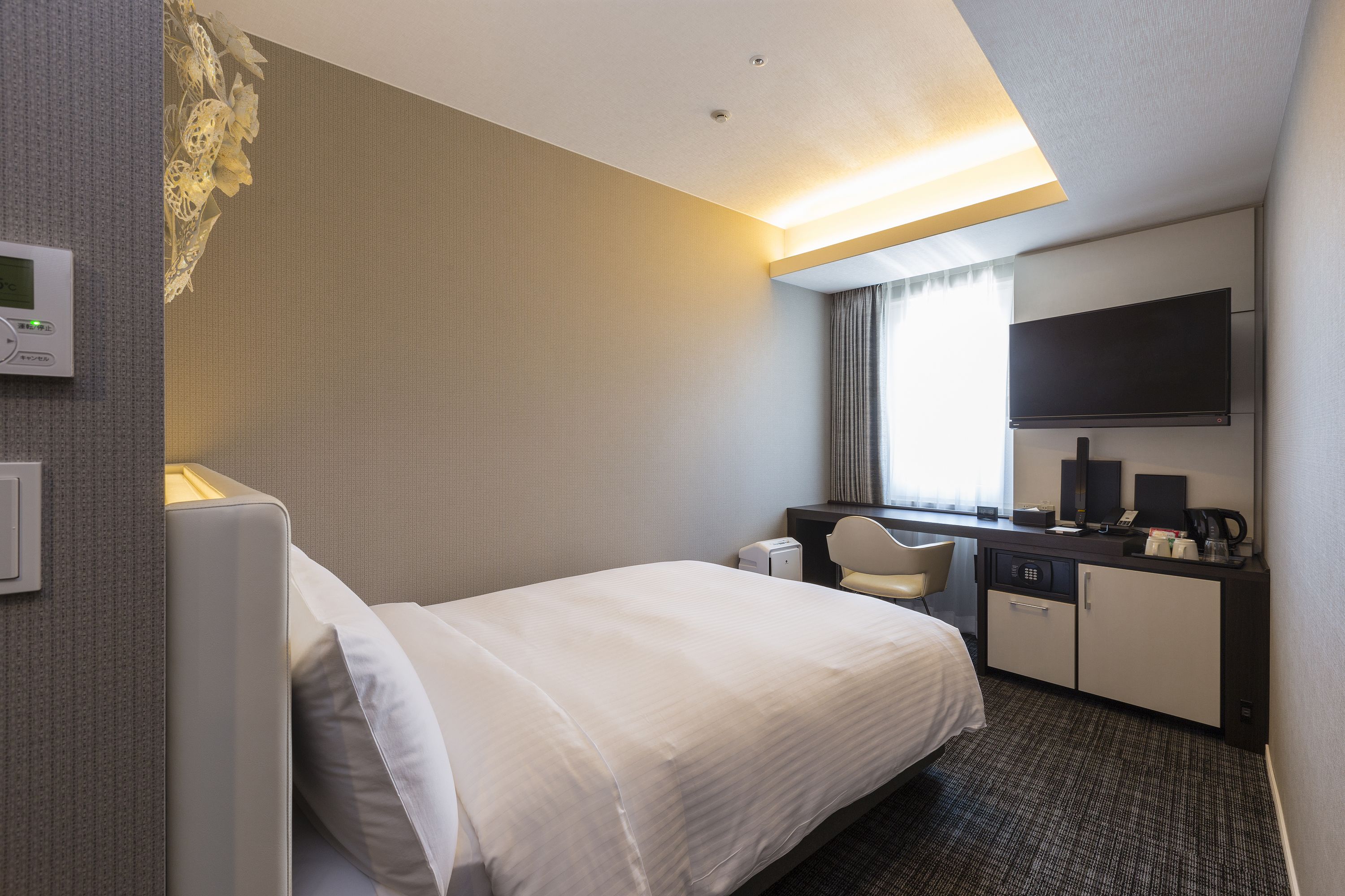 A hotel room with a bed, a desk with a chair, a television, and a coffee maker.