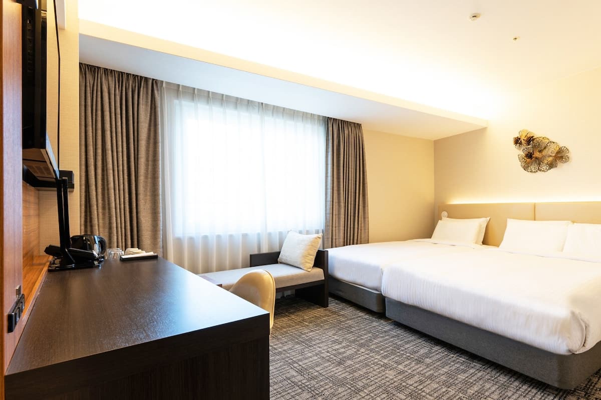 A hotel room with a bed, a desk, a chair, and a large window with curtains.