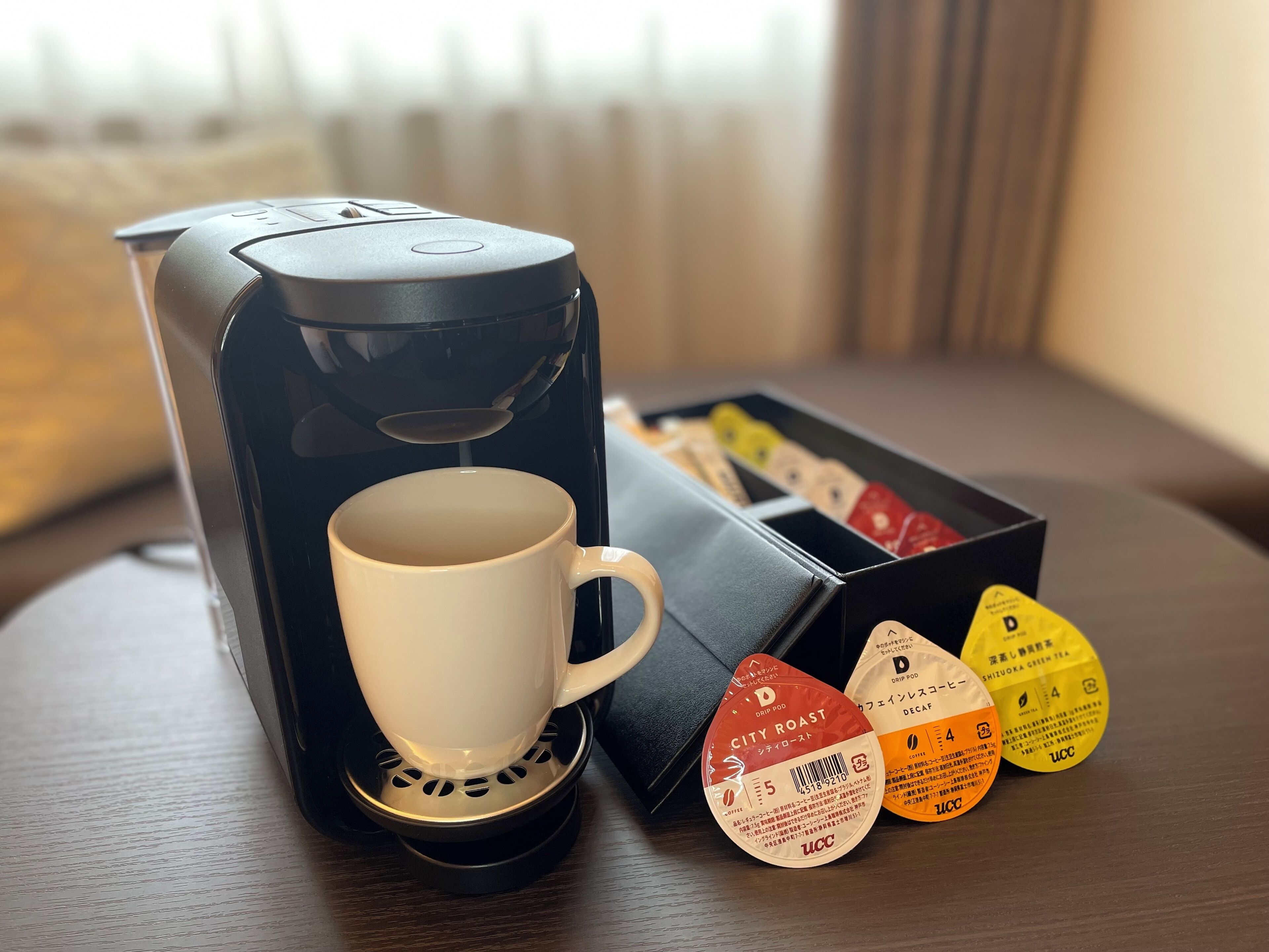 A coffee maker with a cup and a box of tea pods.