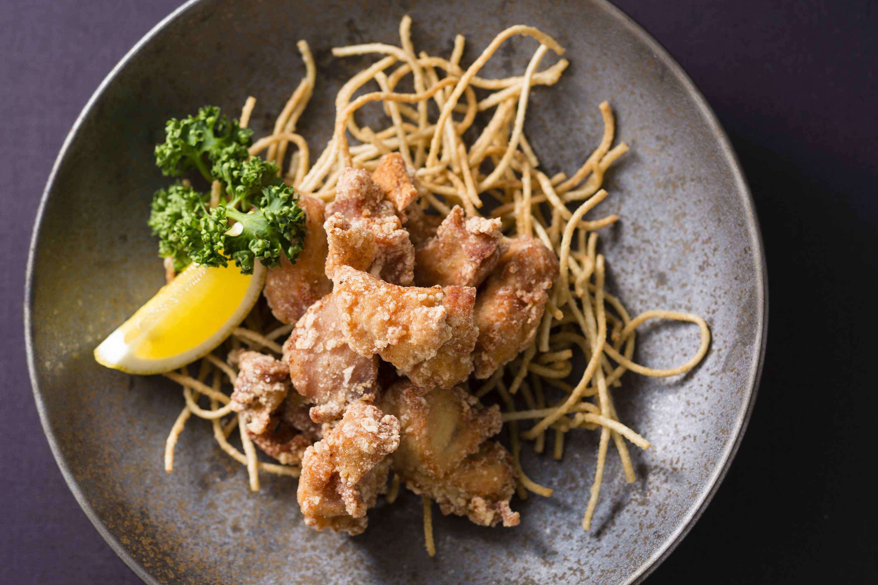A plate of fried chicken and noodles with a lemon wedge and parsley garnish.