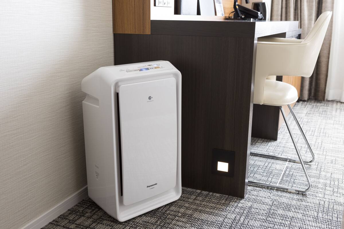 A compact, white portable heater in a hotel room with a dark wooden desk and a white chair.