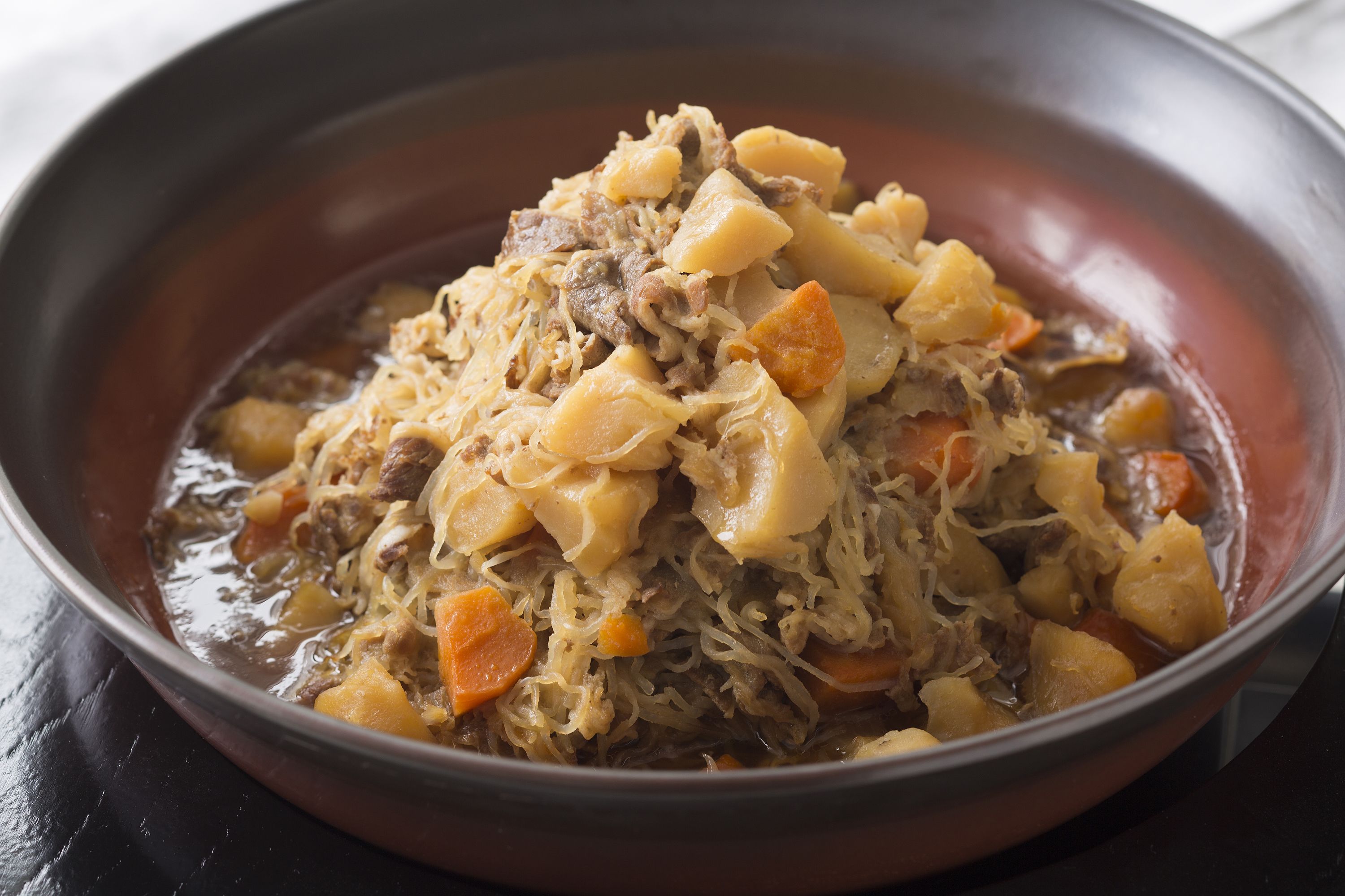 Un bol de ragoût contenant de la viande, des pommes de terre et des carottes.
