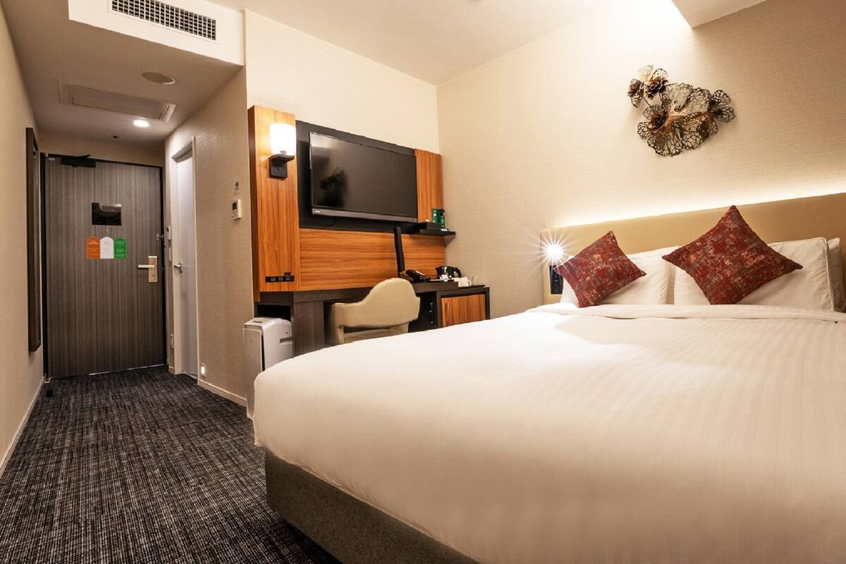 A hotel room with a large bed, a desk, a chair, a television, and a decorative wall piece.