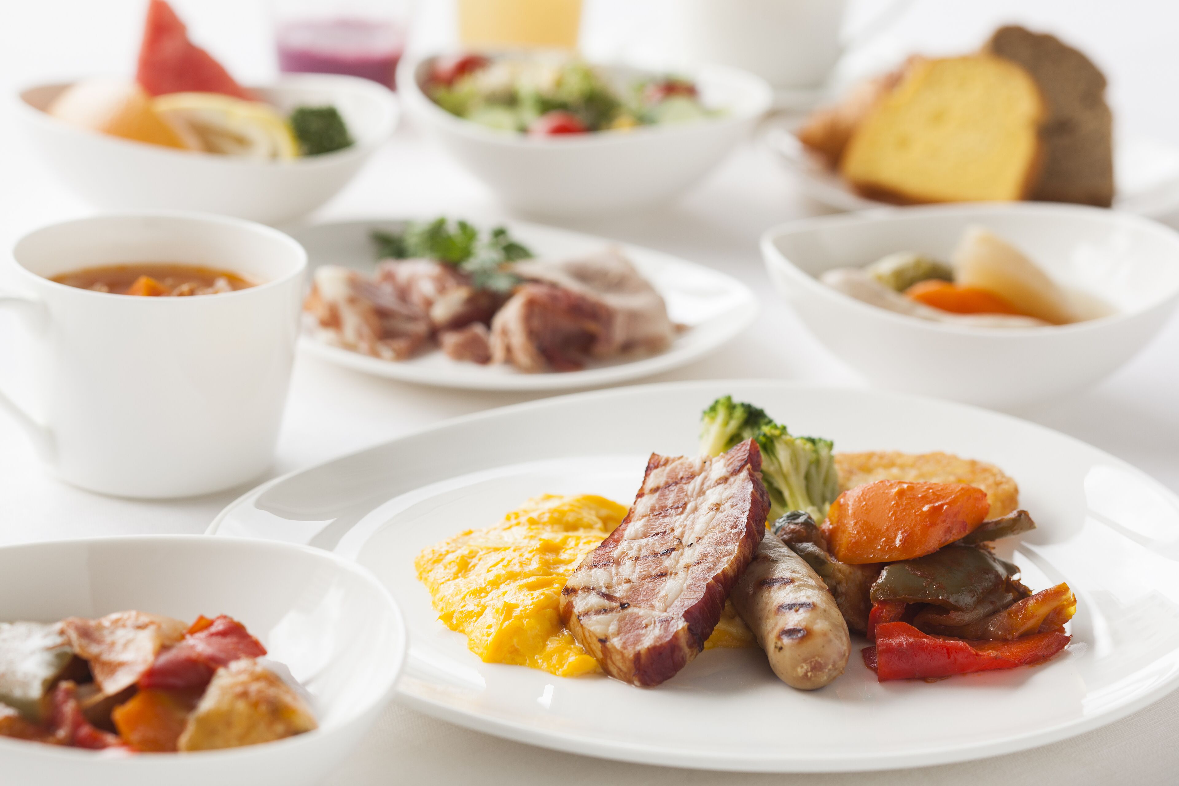 Une variété de plats, notamment de la viande, des légumes et des œufs brouillés, présentés sur une table blanche.
