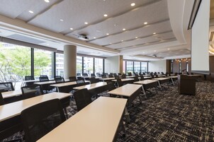 A conference room with rows of tables and chairs, large windows, and a carpeted floor.