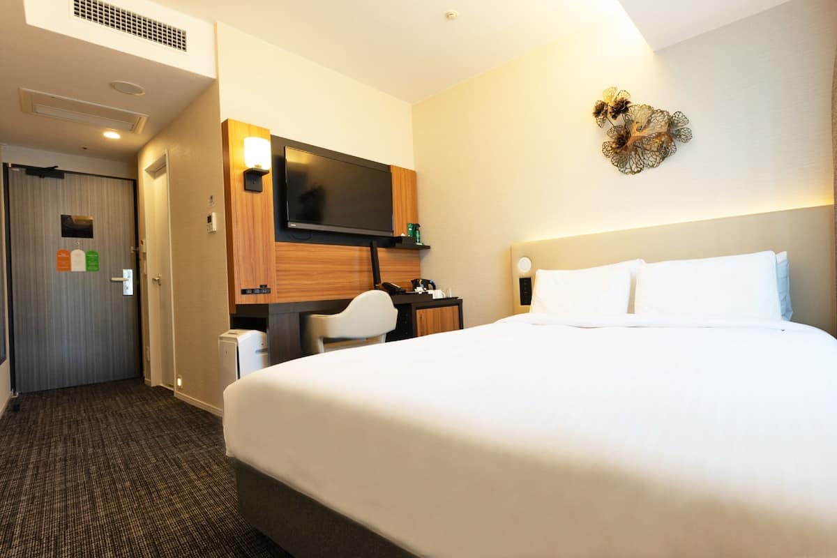 A hotel room with a large bed, a desk, a TV, and a heart-shaped wall decoration.