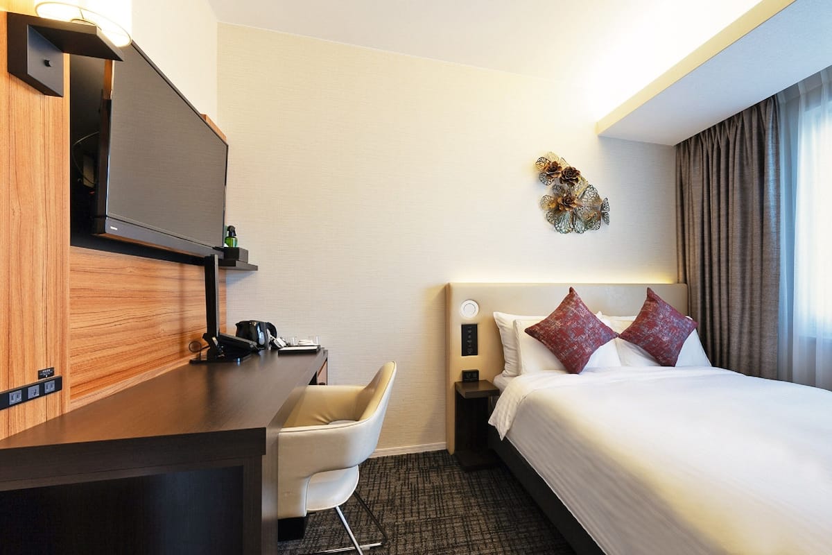 A hotel room with a bed, a desk, a chair, a TV, and a wall decoration.