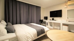 A modern hotel room with a bed, desk, chair, and a flat-screen TV.