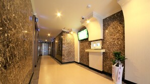 A hotel reception area with marble walls, a reception desk, a television, and a potted plant.