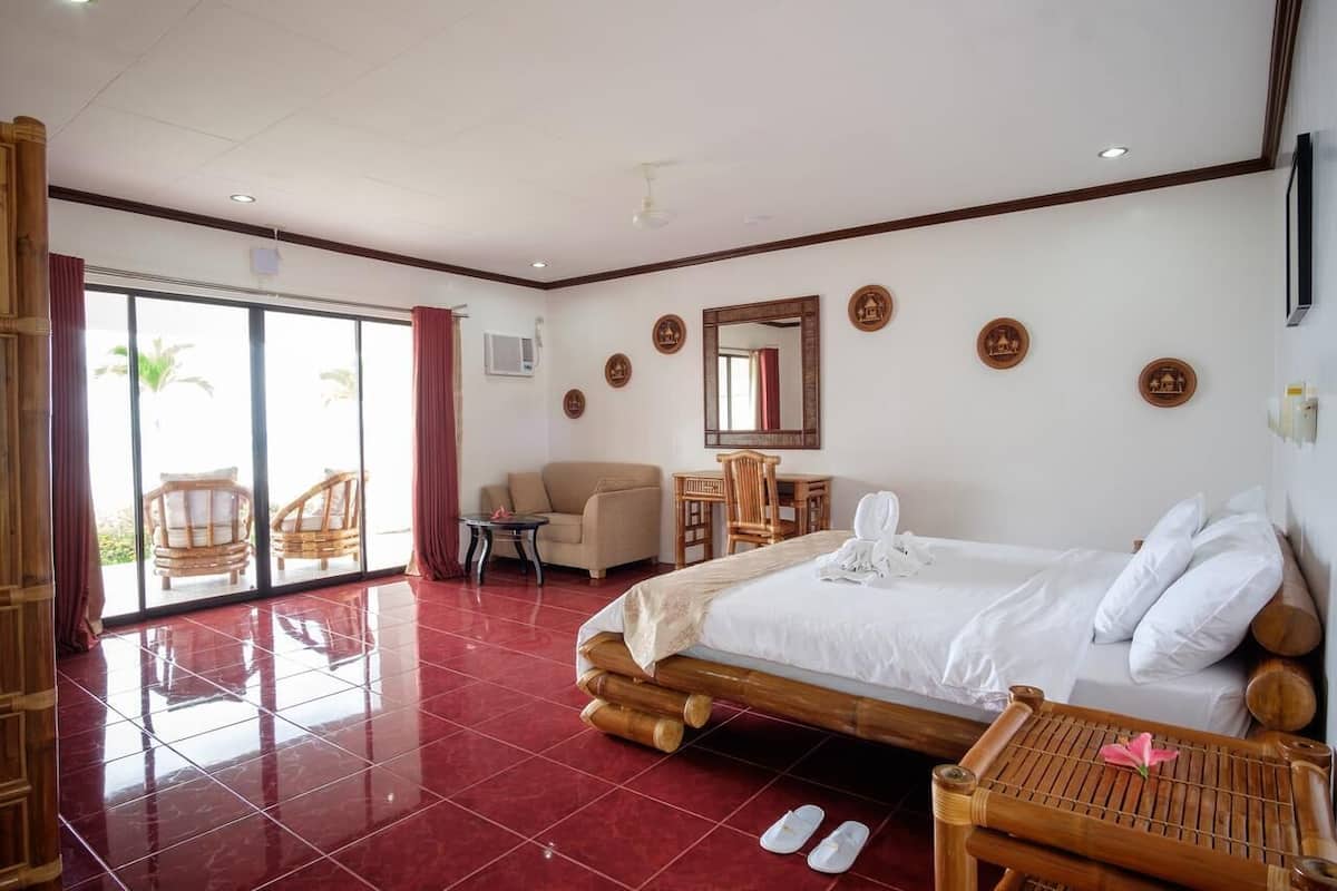 Habitación de hotel con una cama grande, un escritorio, una silla y vistas a través de una puerta corrediza de vidrio.