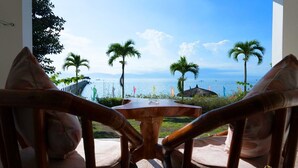 A view from a room with a wooden table and chairs, overlooking a beach with palm trees and a pier.