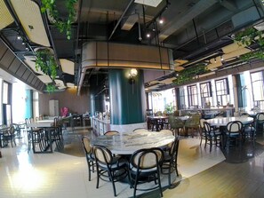 A spacious indoor dining area with multiple round tables and chairs, high ceilings with exposed ductwork, and large windows allowing natural light. - Luminor Hotel Jambi Kebun Jeruk by WH (Jambi)