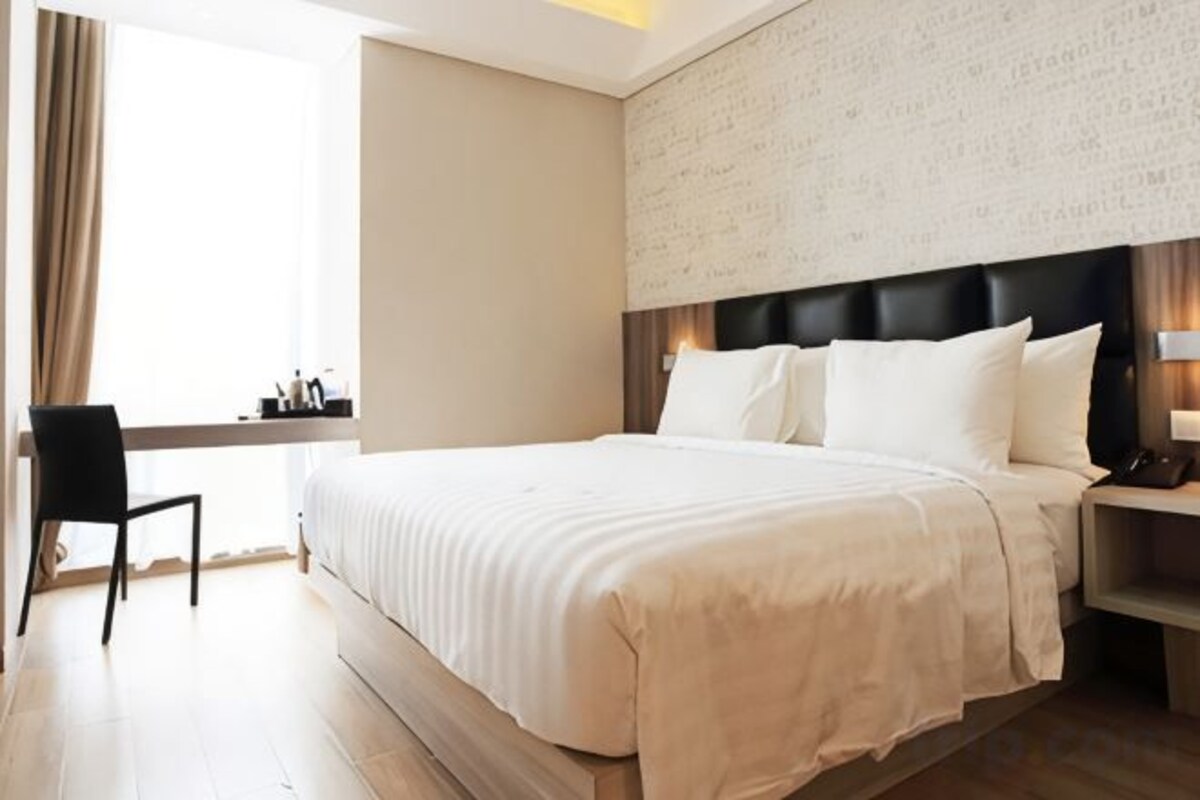 A hotel room with a large bed, a desk, and a chair.