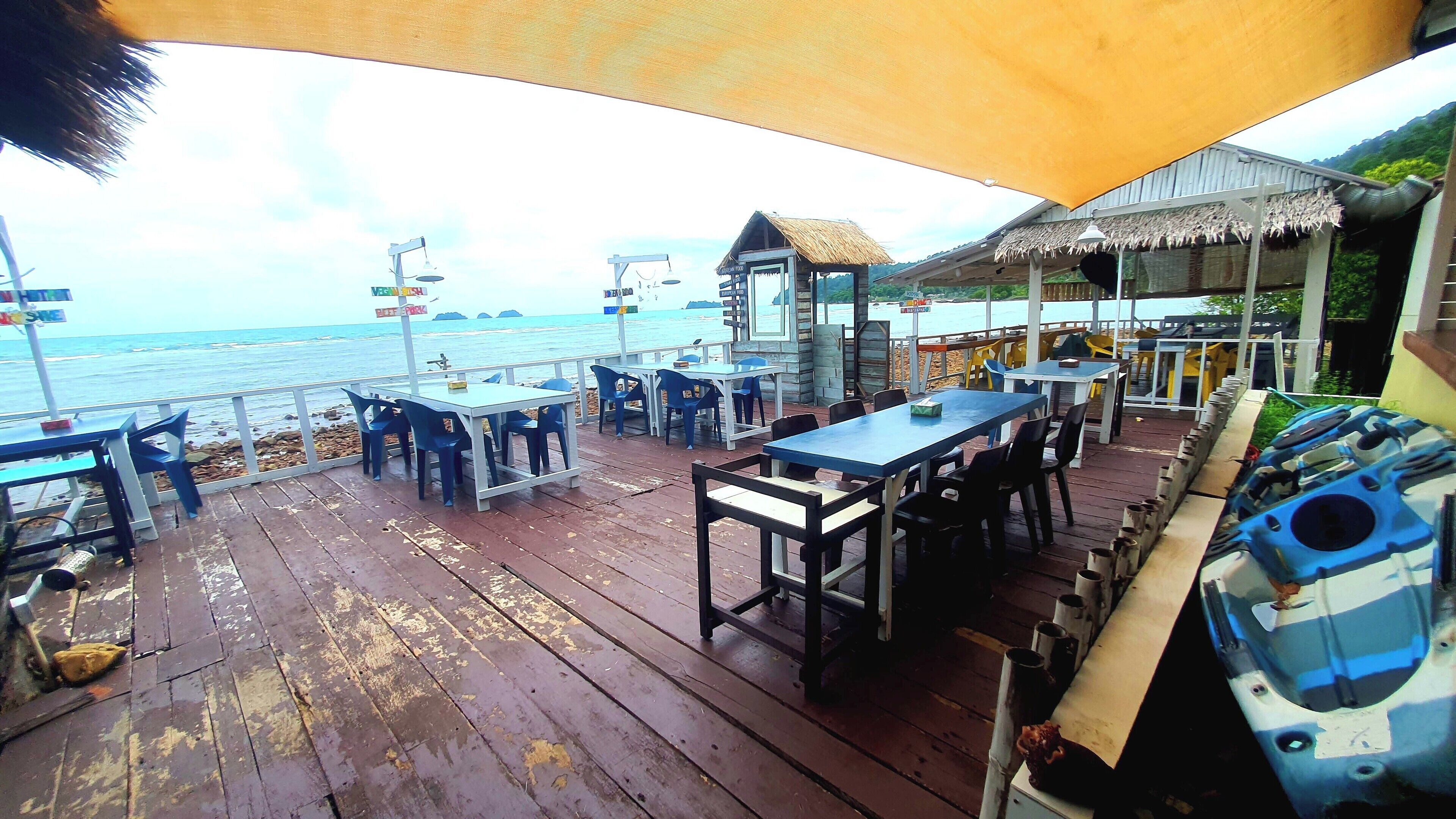 An outdoor dining area with tables and chairs, overlooking the sea.