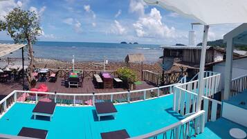 A beachside terrace with a pool, lounge chairs, and a view of the sea.