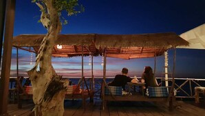 Une terrasse en bois surmontée d’un toit de chaume, avec vue sur la mer.