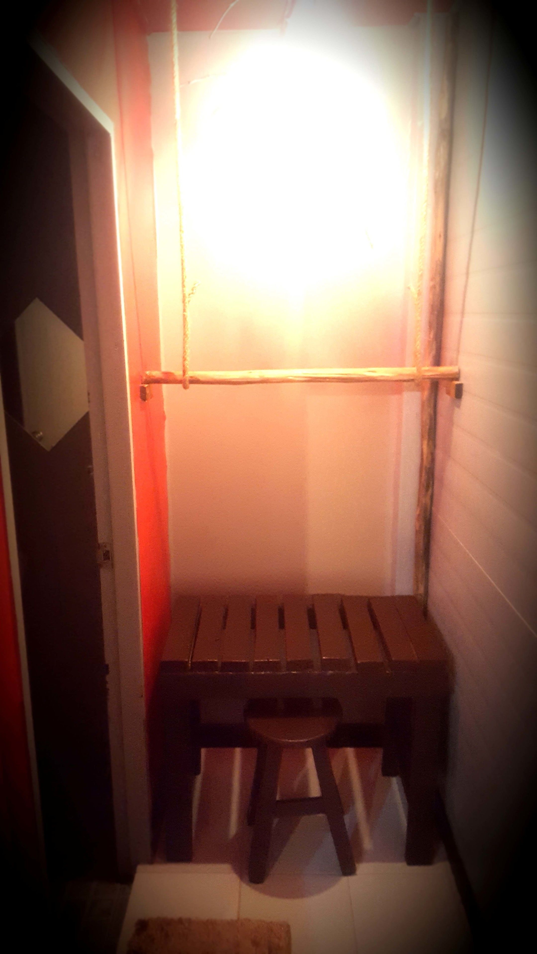 Una habitación pequeña, tenuemente iluminada, con un banco de madera y una sola silla.