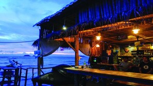 Un bar situé en bord de mer, avec un toit de chaume, offrant une vue sur l’océan.