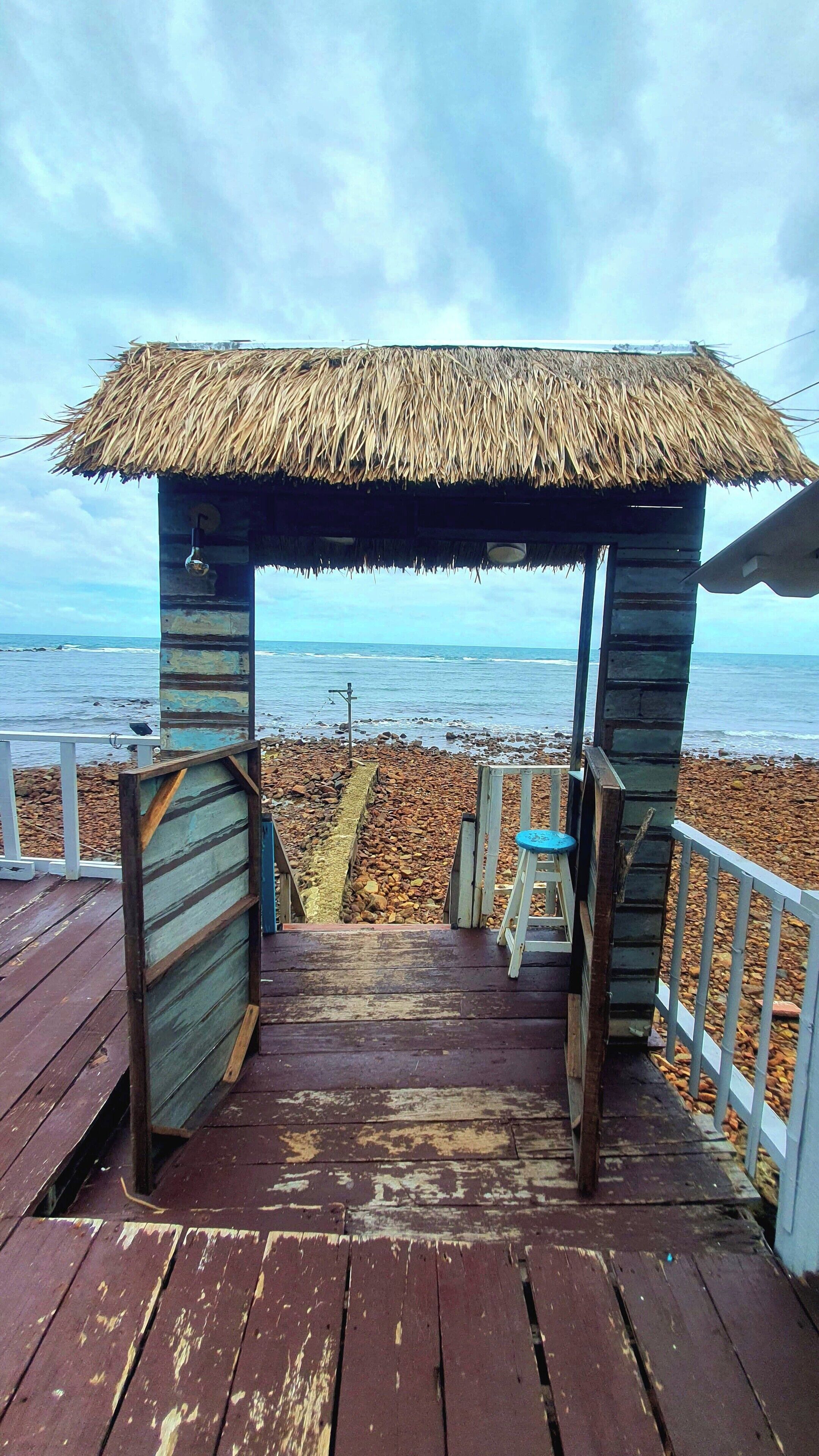 Een houten terras dat leidt naar een rieten dakgebouw met uitzicht op de oceaan.