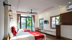 A modern hotel room with a large bed, a desk, and a balcony with a view of palm trees. - Hung Do Beach Homestay (Da Nang)