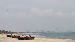 A beach with several boats lined up on the sand, a clear sky, and a distant city skyline. - Hung Do Beach Homestay (Da Nang)