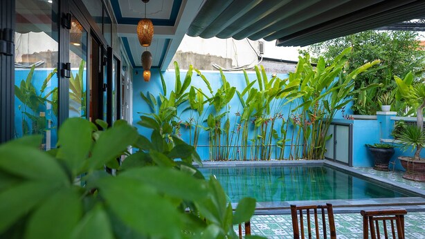 A pool area with a blue wall, potted plants, and wooden chairs. - Hung Do Beach Homestay (Da Nang)