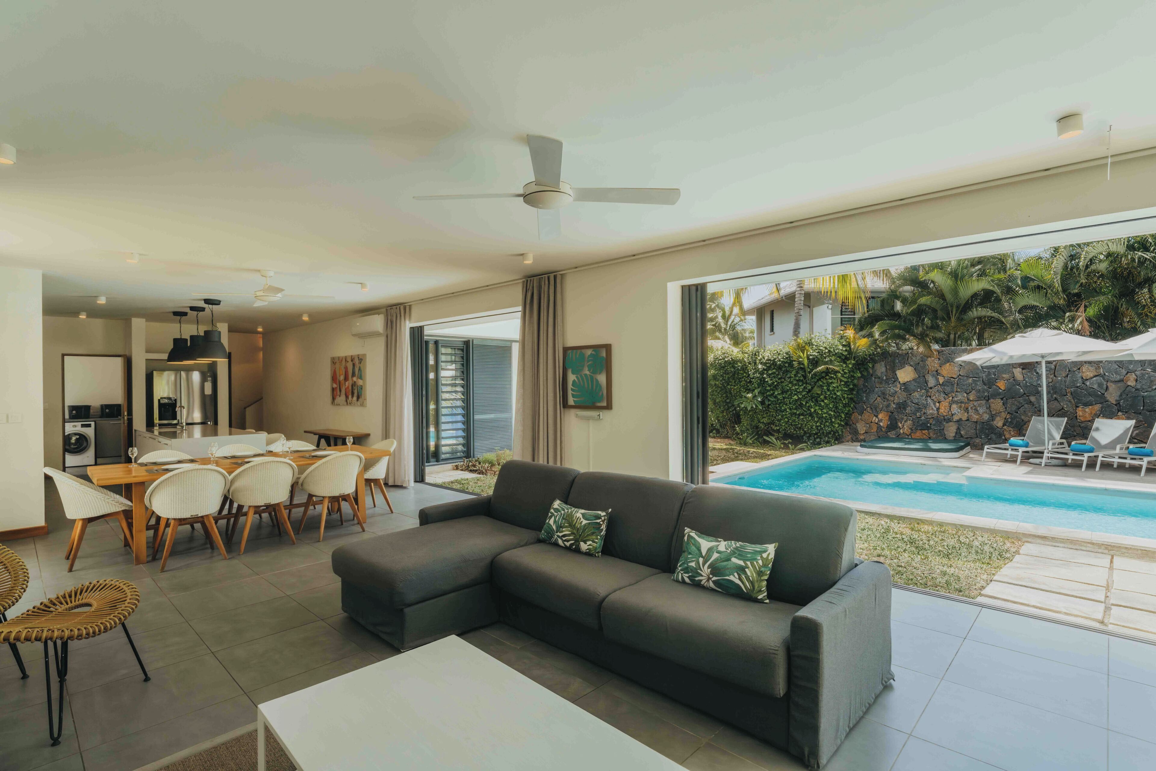 A modern living room with a sectional sofa, dining area, kitchen, and a poolside view.