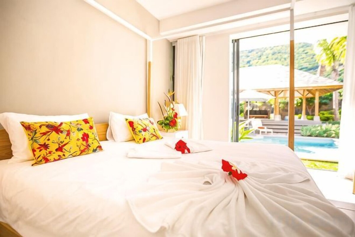 Une chambre d’hôtel avec un grand lit, une vue sur la piscine et un paysage tropical.