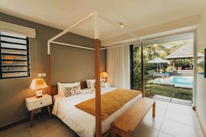 Un dormitorio con cama con dosel, una mesita de noche con lámpara, un banco y vistas a una piscina y zona exterior.