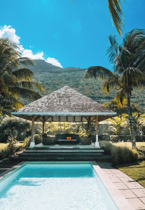 Una piscina con un pabellón, palmeras y montañas al fondo.
