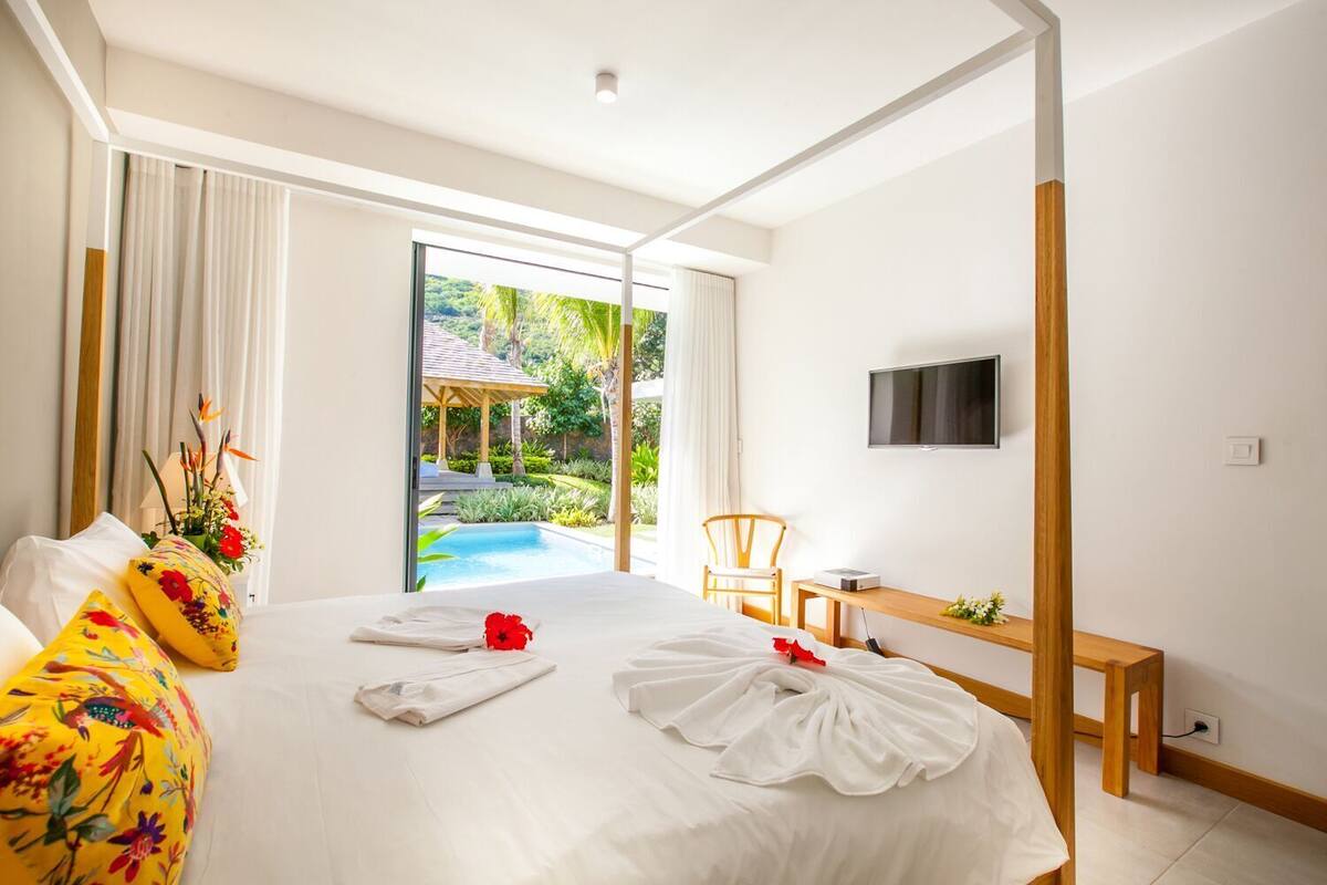 Habitación de hotel con cama, escritorio, silla, televisor y vista a una piscina y jardín.