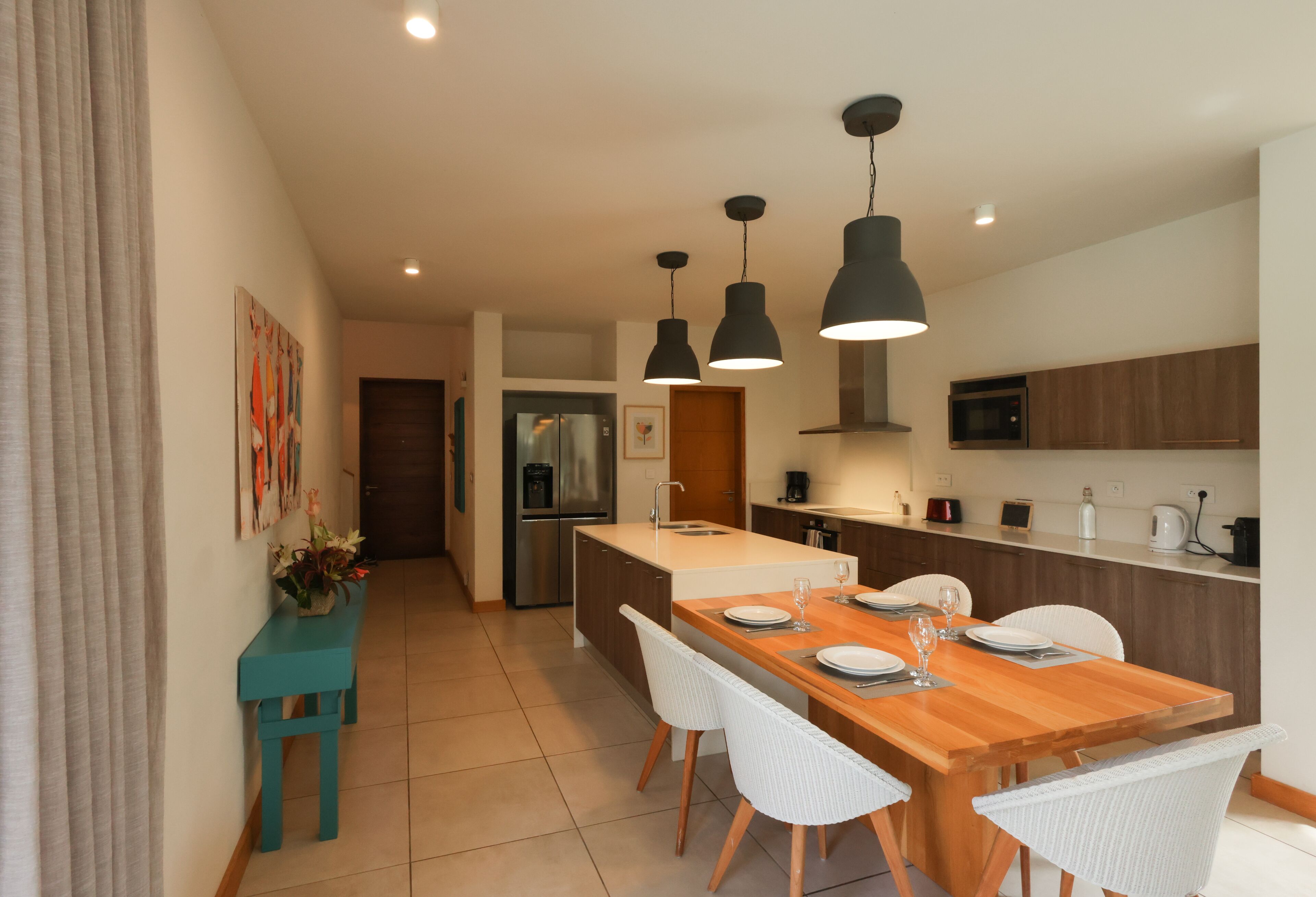 Una cocina moderna con una isla central, sillas blancas e iluminación colgante.