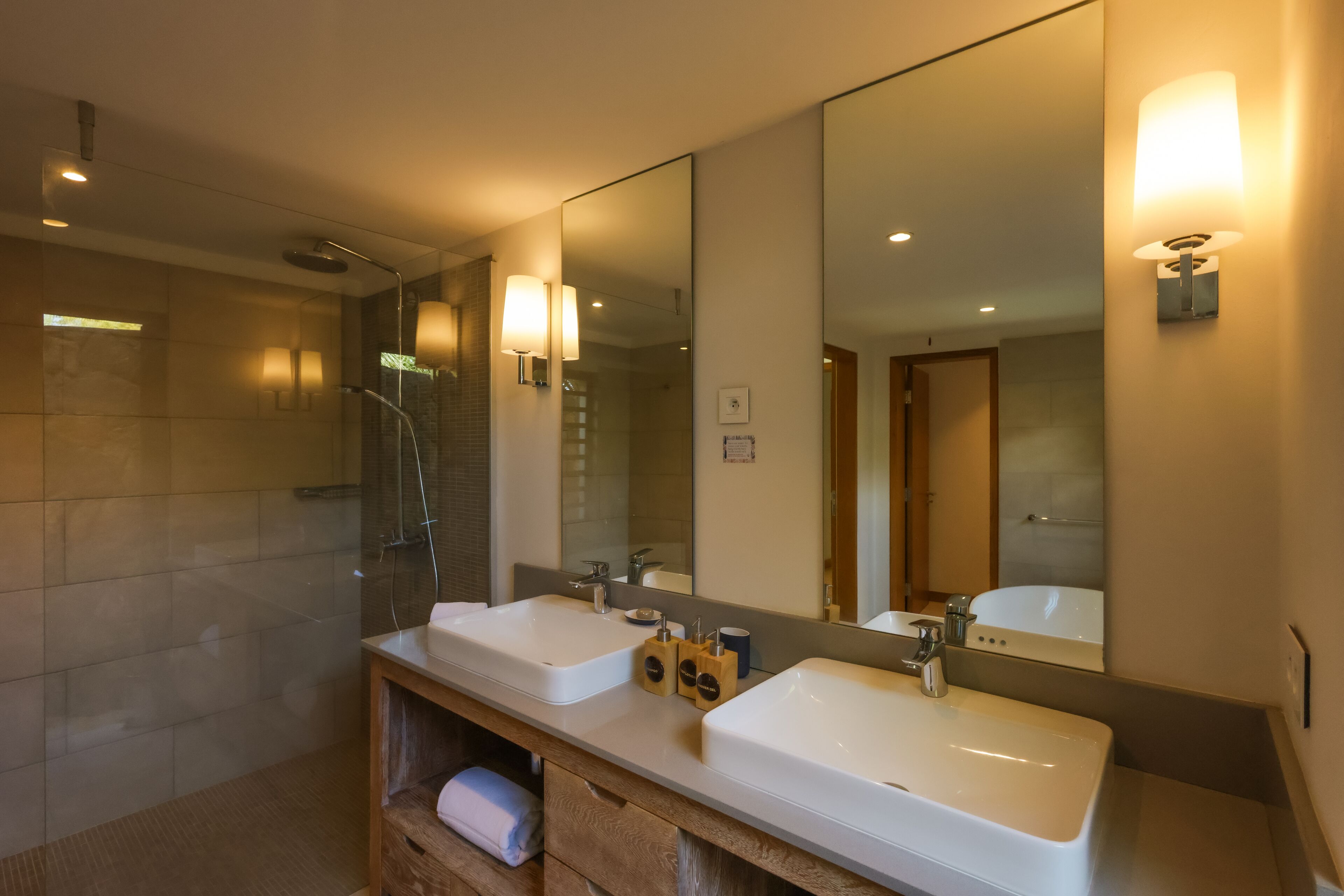 A modern bathroom with two sinks, a large mirror, and a shower area.