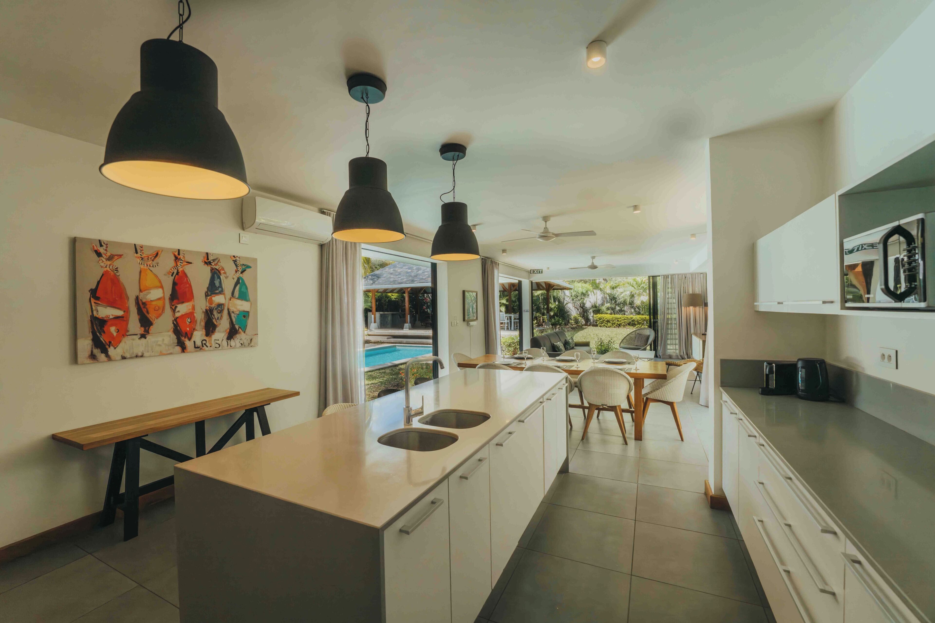 A modern kitchen with pendant lighting, a central island, and a dining area with a view of the outdoors.