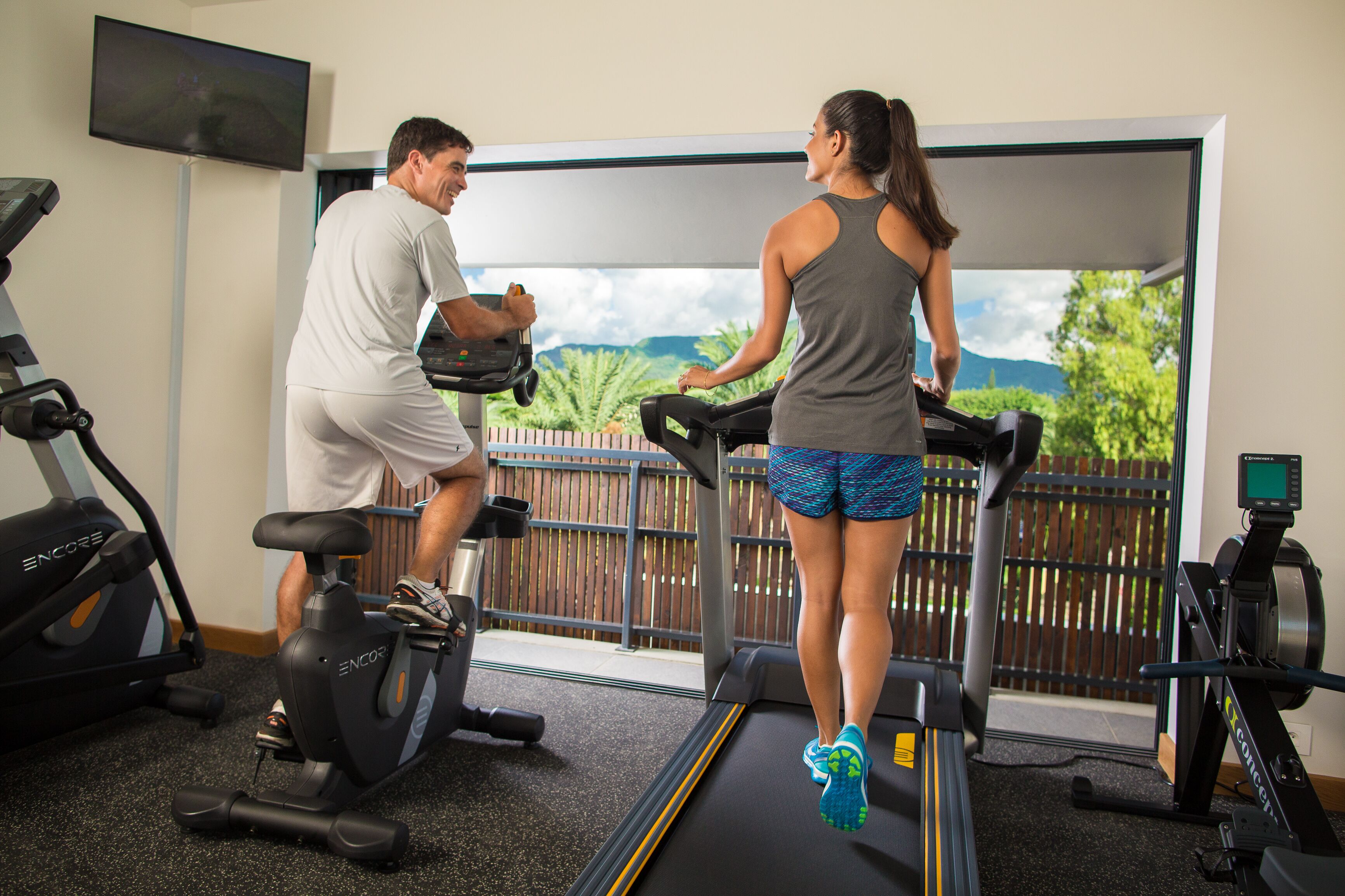 A gym with treadmills, stationary bikes, and a TV on the wall.
